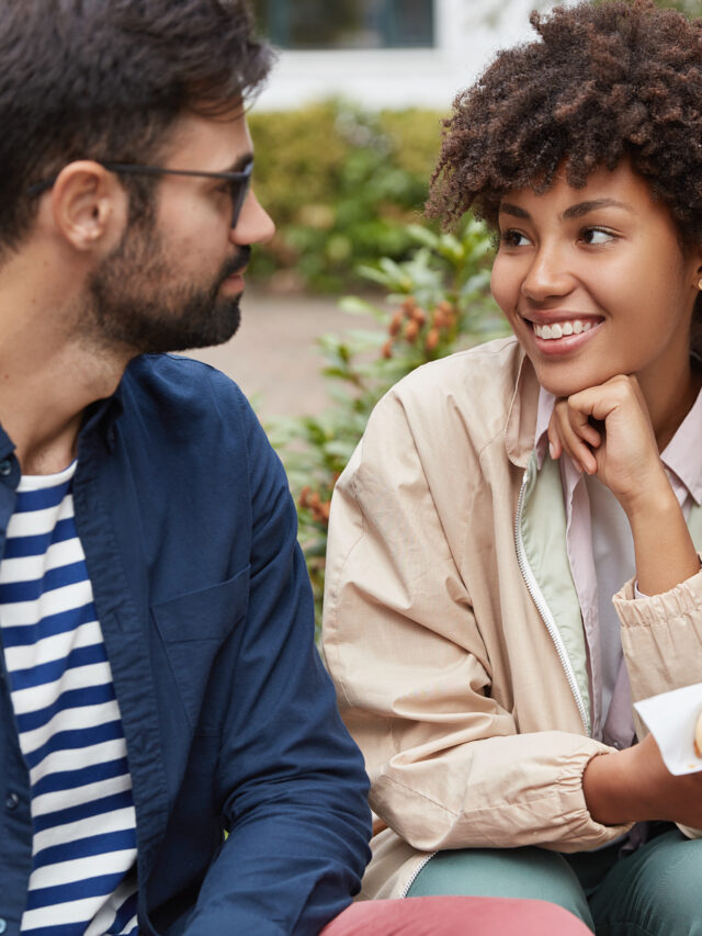 Multiethnic couple have stroll outdoor, rest in city, eat sandwich, look positively at each other, discuss future plans. Groupmates eat fast food after classes. City life and leisure time concept